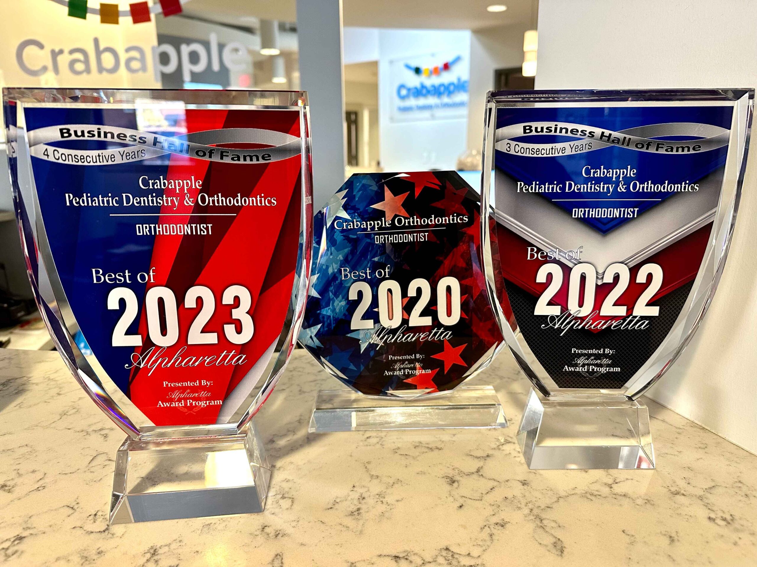 Three dental practice awards displayed on marble counter, years 2020, 2022, and 2023.