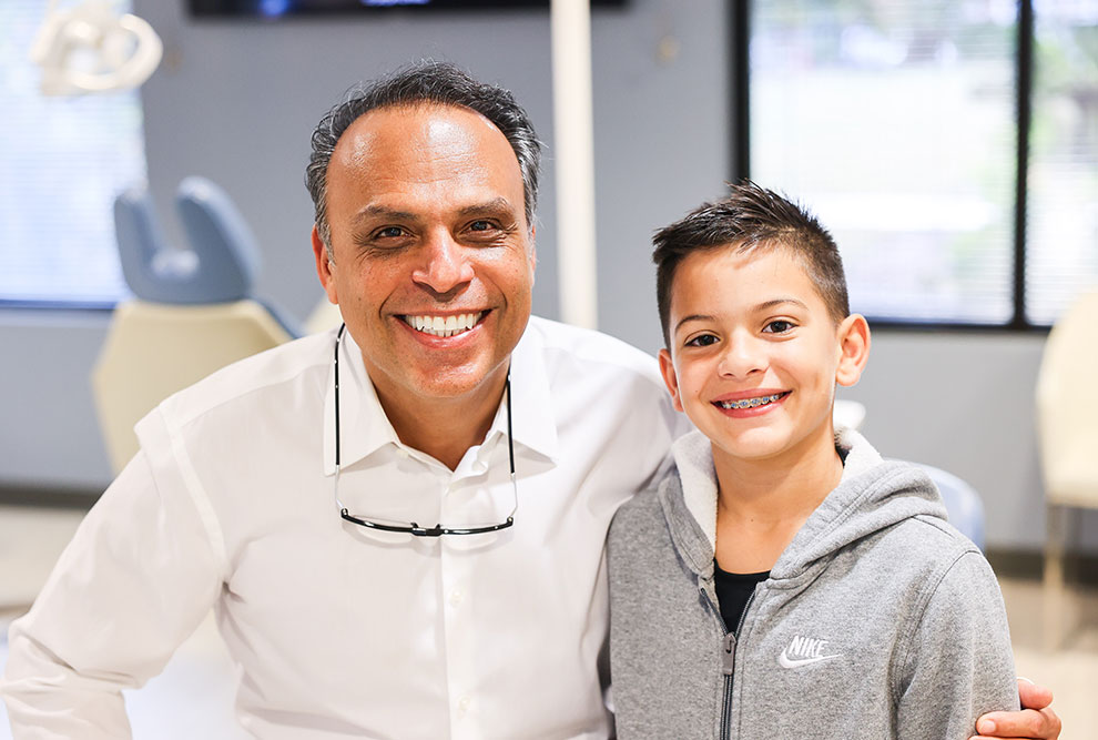 Adult dentist and young child smiling together in modern dental office setting.