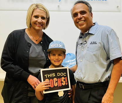 Young child holding sign with two adults at pediatric dental office event or celebration.