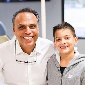 Adult dentist and young boy smiling together in pediatric dental office setting.