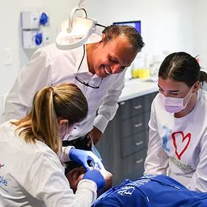 Three pediatric dental professionals examining a young patient in a modern dental clinic setting.