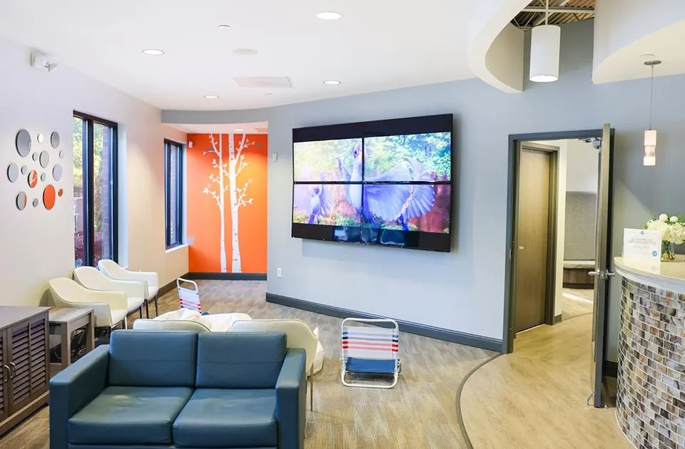 Modern pediatric dental office waiting room with blue couch, wall-mounted TV, and contemporary decor.