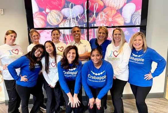 Dental team members wearing blue branded shirts posing together in office with colorful floral display.