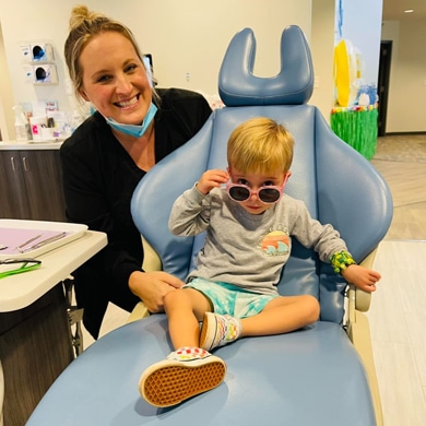 Pediatric dentist with young child patient wearing sunglasses in dental chair at office.
