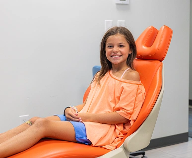 Young girl smiling in orange dental chair at pediatric dentistry office