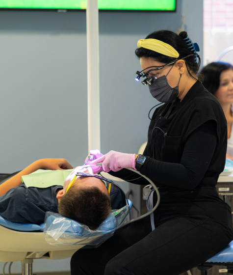 Dental professional wearing mask and gloves examining young patient in clinical treatment room.