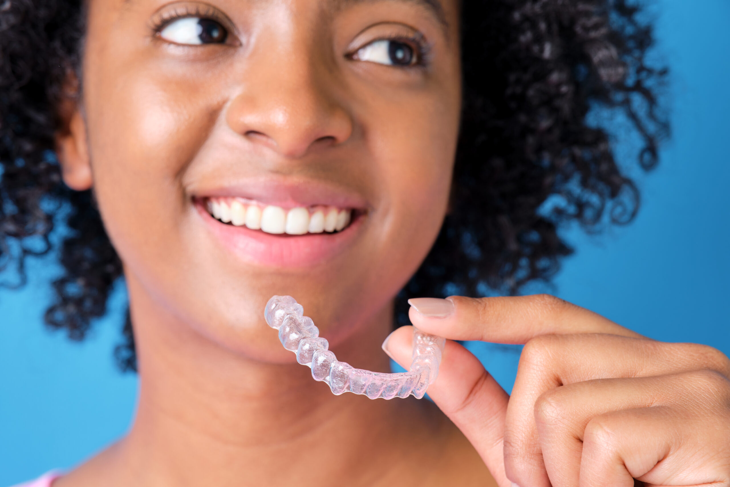 A woman smiles while holding an Invisalign aligner, showcasing her confidence in her orthodontic treatment