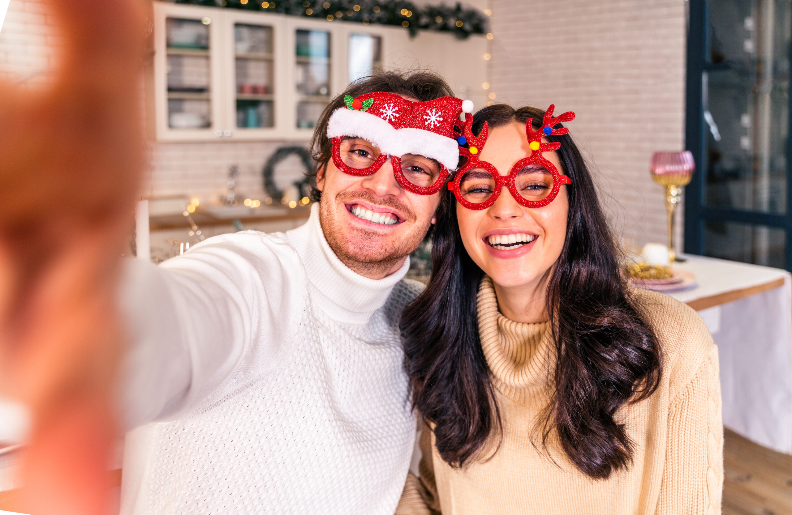 A man and woman wearing festive Christmas glasses pose together for a cheerful selfie.